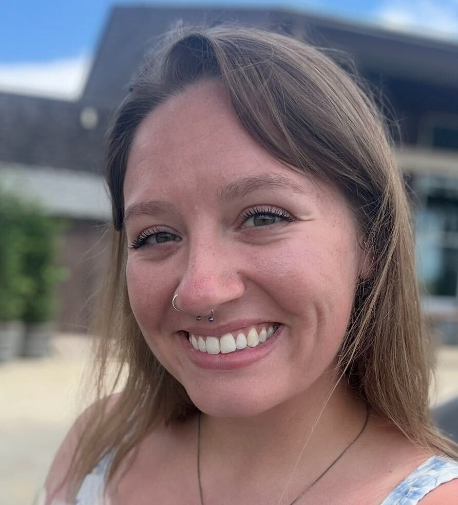 Smiling woman with a nose hoop and two tiny nasal studs, outdoors on a sunny day.