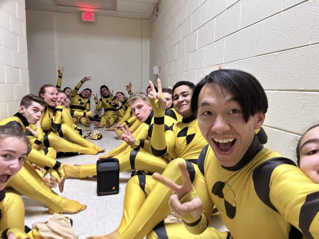 wg-about-2 - MBI Arts MBI Winter Guard members in crash test dummy costumes celebrating together backstage