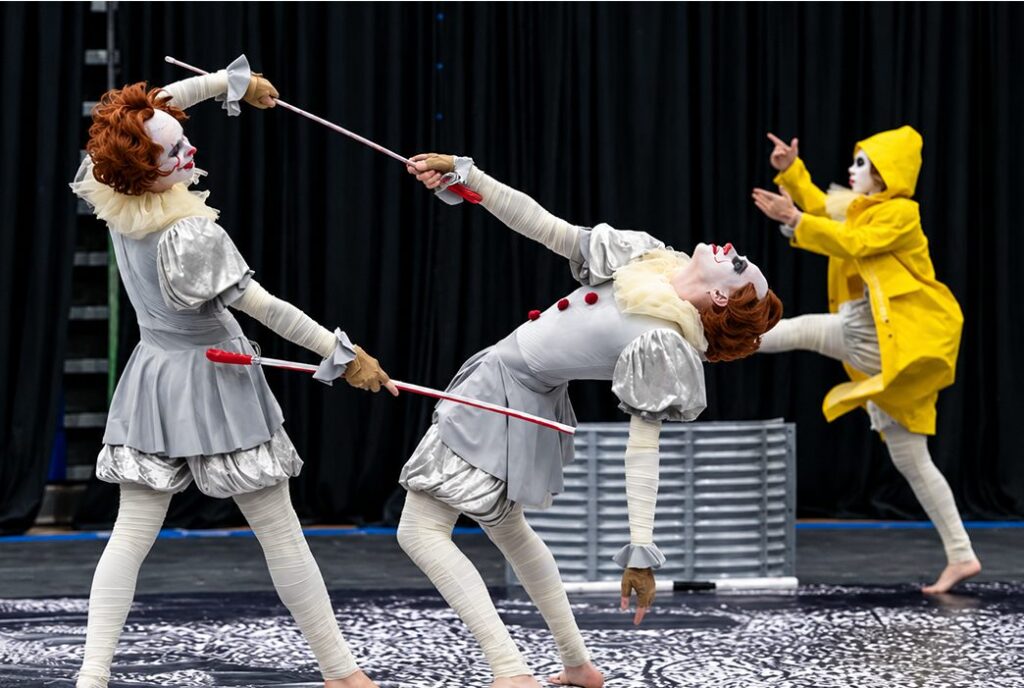 wg-about-2-v2 - MBI Arts Three MBI Winter Guard performers in clown and raincoat costumes during the 2023 show Welcome to Derry