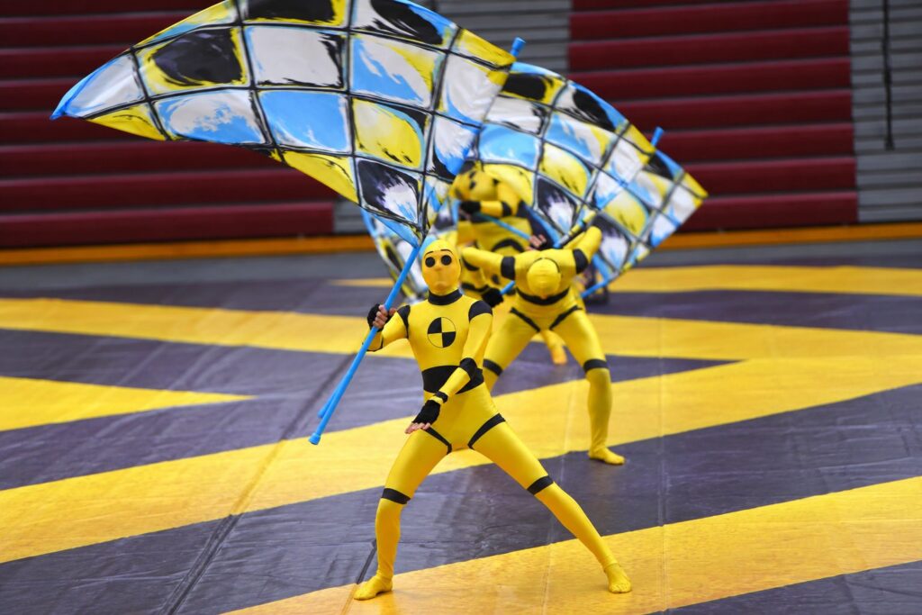 An MBI Winter Guard performer spinning a checkered flag during the 2024 show Shut Up and Drive