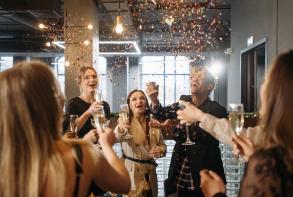 Group of friends toasting with champagne in a celebratory party as confetti falls around them indoors.